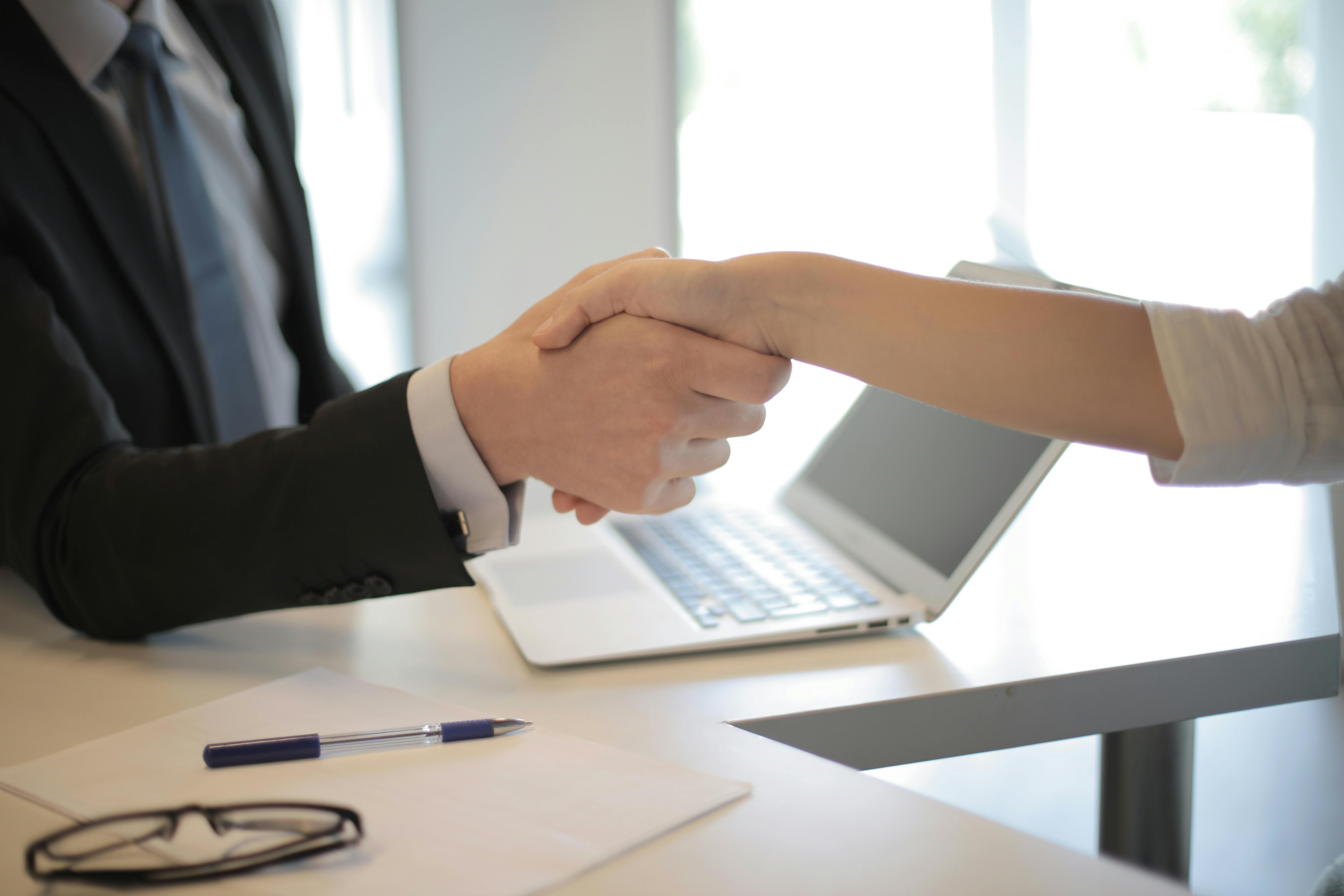 Two people shaking hands across an office desk.